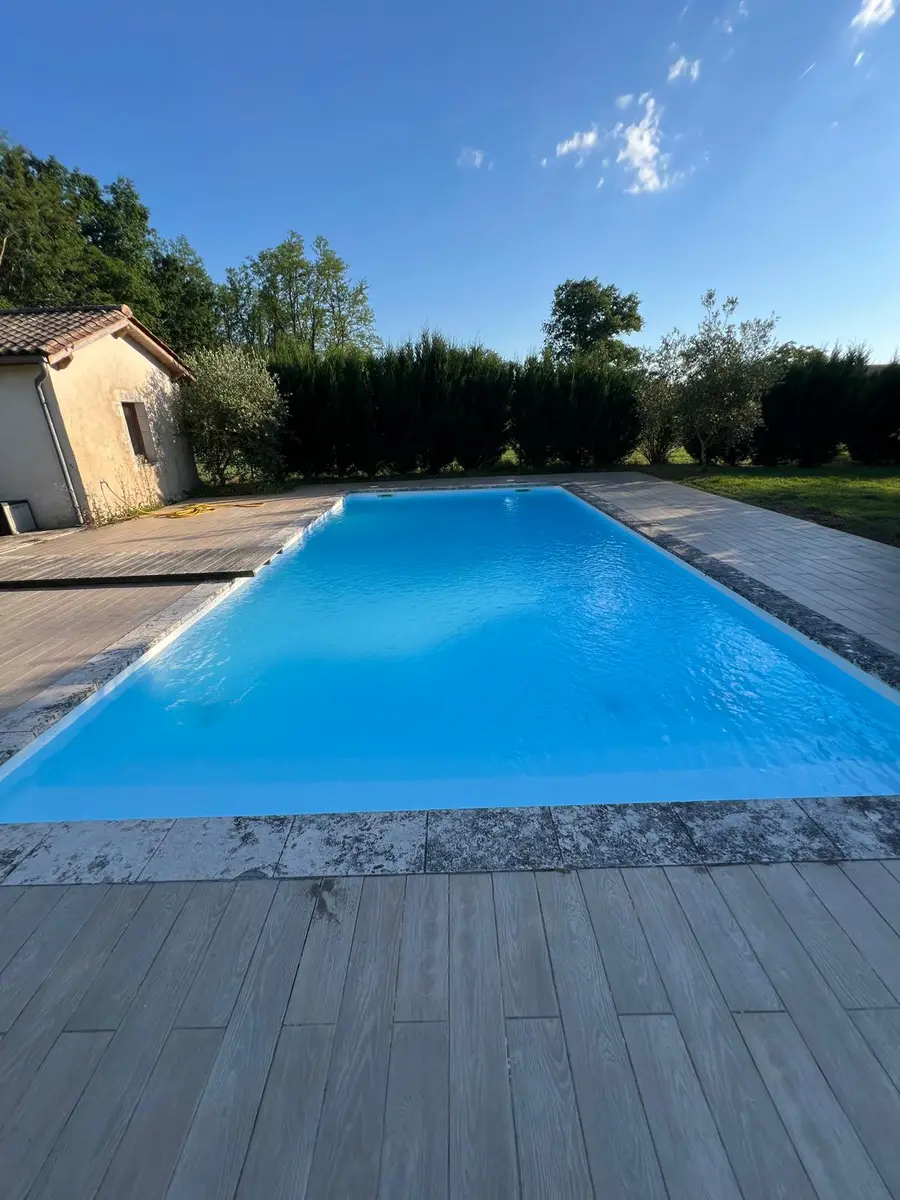 Belle piscine aux reflets bleus sur terrasse bois par beau temps — résidence secondaire bien entretenue